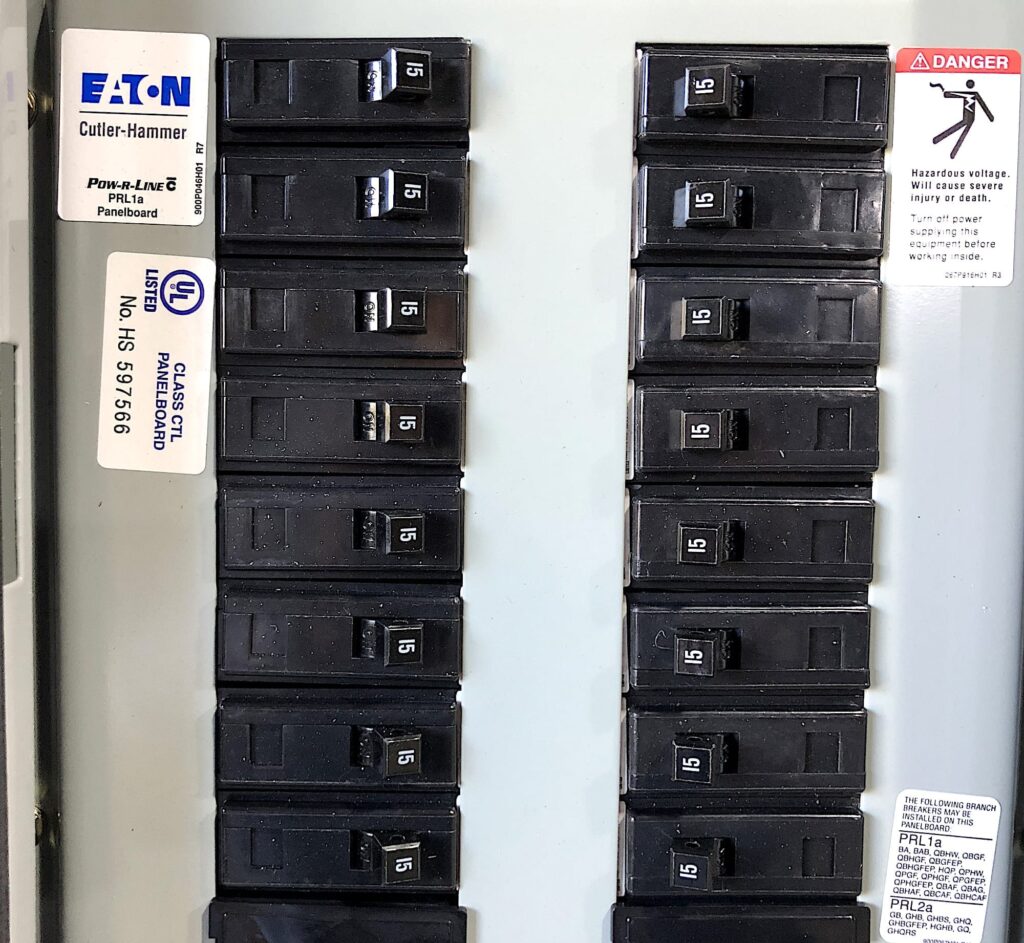 Modern Eaton Cutler-Hammer electrical breaker panel with labeled 15-amp switches and safety warning label — example of a grounded residential panel meeting current electrical codes.