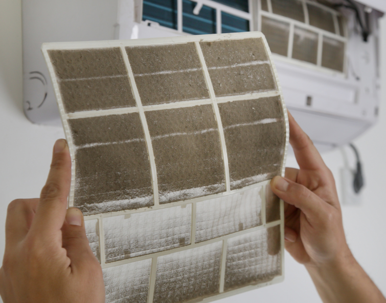 Hands holding a dirty, heavily clogged air filter removed from an indoor heating unit