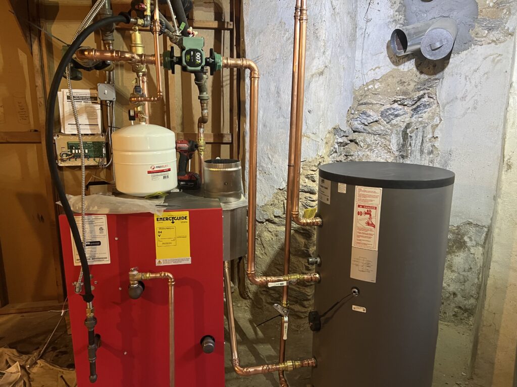 New high-efficiency red gas boiler and indirect water heater tank installed by GEN3 in a Philadelphia stone basement with overhead copper piping.